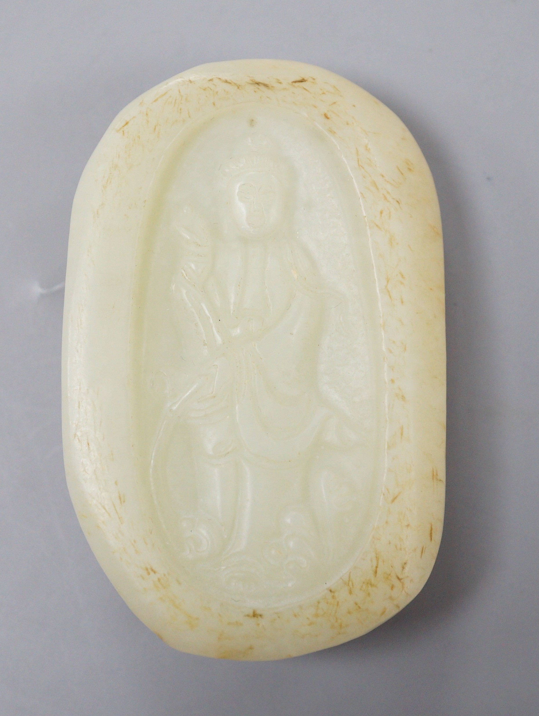 A Chinese celadon jade pebble carving depicting Guanyin, 7.5cm tall